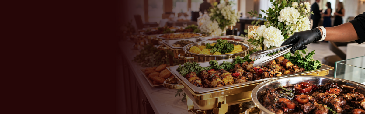 Elegant catered buffet with assorted dishes, gold serving-ware, and fresh floral arrangements.